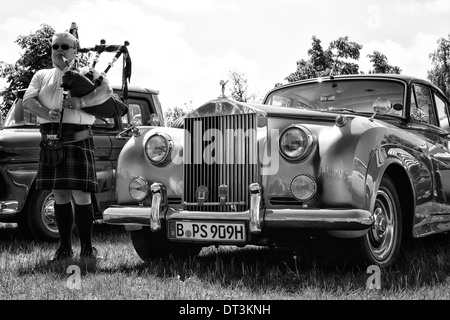 Piper spielt die Great Highland Bagpipe in der Nähe der Auto Rolls-Royce Silver Cloud Stockfoto