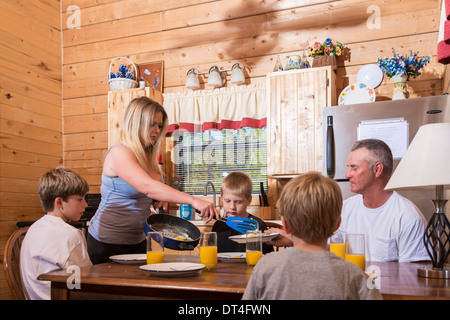 Mutter, Vater und 3 jungen am Frühstückstisch in der Küche. Die Frau ist Spiegelei zum Frühstück serviert. Stockfoto