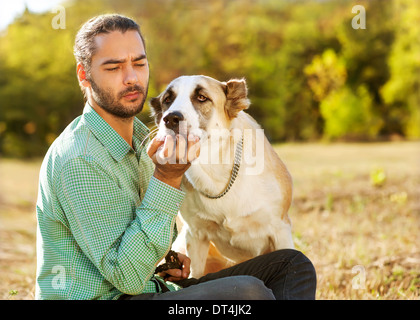 Mann und zentraler Asiatischer Schäferhund spazieren im Park. Er hält den Hund an der Leine. Stockfoto