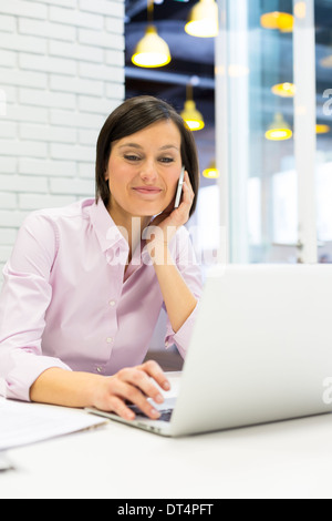 Brunette Geschäftsfrau auf dem Handy mit Computer im Büro Stockfoto