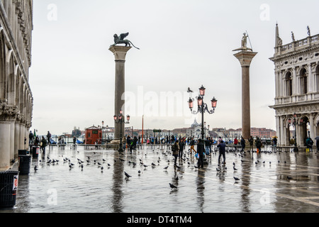 Venedig, Italien. Blick über die Piazzetta di San Marco mit zwei Spalten und Touristen in Regenkleidung Tauben füttern, an einem regnerischen Tag. Stockfoto