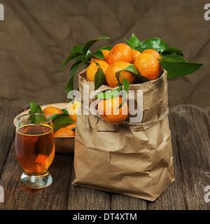 Frische Mandarinen in recyceln Papiertüte und Glas Saft auf Holztisch. Closeup. Stockfoto