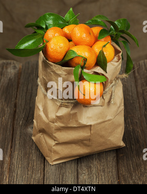 Frische Mandarinen mit Blättern in recyceln Papiertüte auf Holztisch. Stockfoto