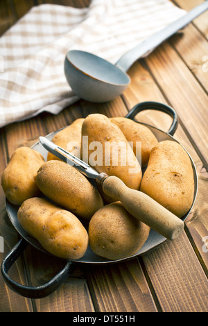 hölzerne Schäler und Kartoffeln auf Holztisch Stockfoto