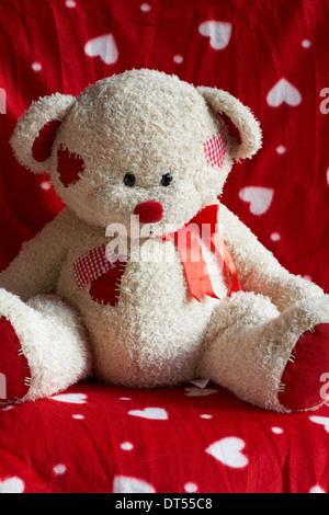 Weiches Kuscheltier Teddybär sitzt auf rote und weiße Herzen Hintergrund Stockfoto