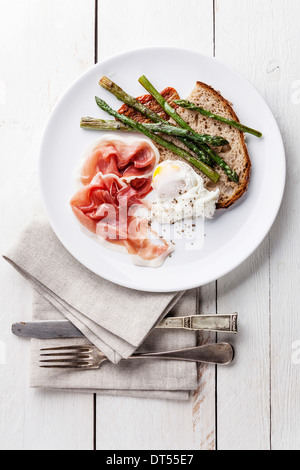 Frühstück mit pochiertem Ei, Parma und Spargel auf weißem Holz Hintergrund Stockfoto