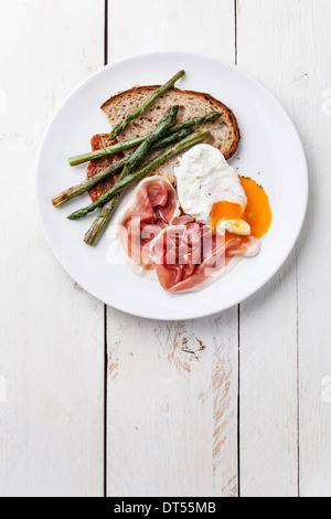 Frühstück mit pochiertem Ei, Parma und Spargel auf weißem Holz Hintergrund Stockfoto