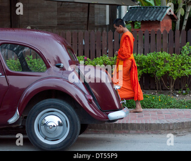 Ein buddhistischer Mönch geht vorbei an einem Oldtimer während morgen Prozession von Almosen in Luang Prabang, Laos. Stockfoto