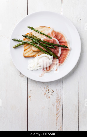 Frühstück mit pochiertem Ei, Parma und Spargel auf weißem Holz Hintergrund Stockfoto