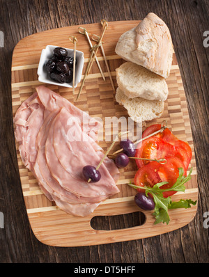 Geschnittene Mortadella auf Kochen Holzbrett mit Brot, Tomaten und Oliven Stockfoto