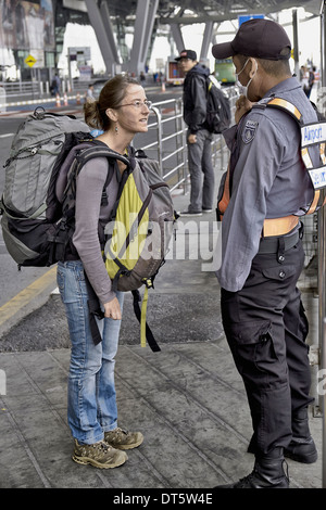 Backpacker-Frau, die am Flughafen Bangkok ankommt und vom Sicherheitsbeamten nach dem Weg sucht. Bangkok Thailand S. E. Asien Thailand Tourismus Stockfoto