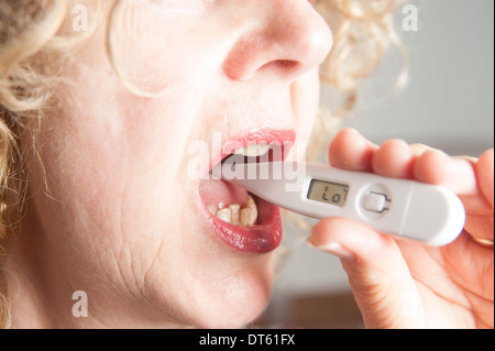 Frau, die ihr eigenes digitales Thermometer mit Temperatur Stockfoto