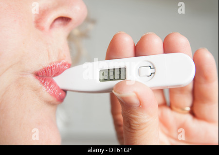 Frau, die ihr eigenes digitales Thermometer mit Temperatur Stockfoto