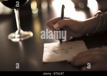 Nahaufnahme der jungen Frau schreibt ihre Telefonnummer auf einer Serviette in der Bar Stockfoto