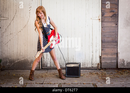 Junge Frau spielt e-Gitarre außerhalb garage Stockfoto