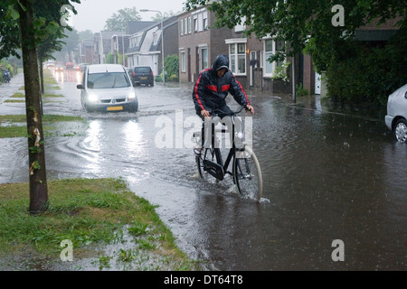 Ein Mann auf einem Fahrrad reitet durch das Wasser nach einem Regenguss Stockfoto
