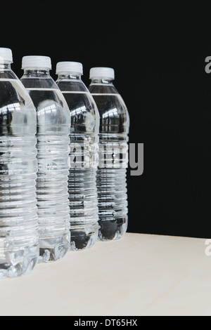 Reihe von klaren, Kunststoff Flaschen mit Wasser gefüllt mit gefiltertem Wasser in Folge. auf einem schwarzen Hintergrund.