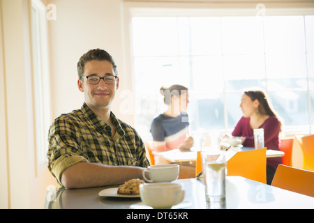 Ein junger Mann sitzt an einem Coffee-Shop-Schalter mit zwei Frauen im Hintergrund. Stockfoto