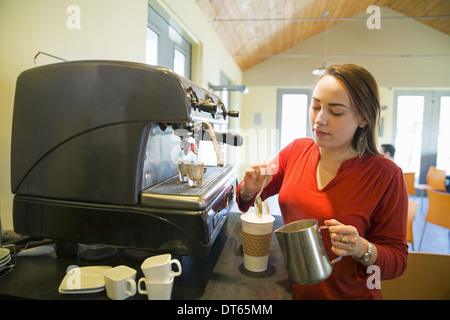 Eine junge Frau, die Zubereitung von Kaffee mit einem großen Kaffee-Maschine. Aufgeschäumten Milch gießen in eine Tasse. Stockfoto