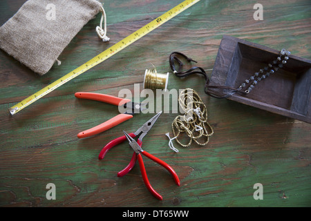 Eine Tischplatte mit Schmuckherstellung Ausrüstung. Zangen, Faden und ein Holztablett mit Maßband. Stockfoto