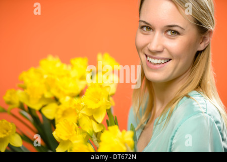 Lächelnde Frau mit gelben Narzissen Frühlingsblumen auf orangem Hintergrund Stockfoto