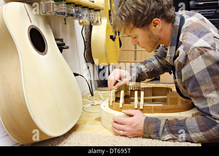 ein junger Mann, der ein Gitarrenbauer ist, macht Akustikgitarre aus Holz in seiner heimischen Werkstatt handgefertigt. Stockfoto