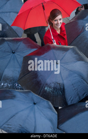 Junge Frau mit roten Regenschirm unter schwarzen Regenschirm Stockfoto