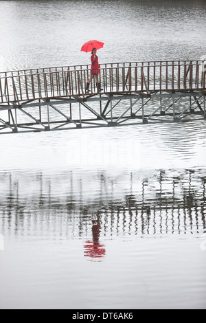 Junge Frau in roten Kreuzung Fußgängerbrücke in Regen Stockfoto