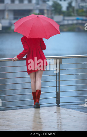 Junge Frau in rot warten von waterfront Stockfoto