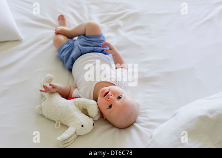 Babymädchen liegt auf Bettwäsche mit Stofftier Stockfoto