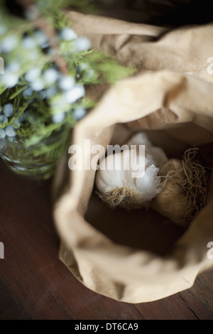 Bio-Zutaten auf den Tisch. Knoblauch Zwiebeln in eine braune Papiertüte. Eine Pflanze mit blauen Blüten. Frische Zutaten. Stockfoto