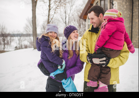 Mutter und Vater tragen Töchter im Schnee Stockfoto