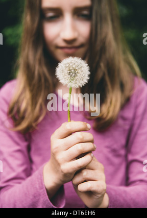 Ein zehn Jahre altes Mädchen hält ein Löwenzahn Uhr Seedhead an einem langen Stiel. Stockfoto