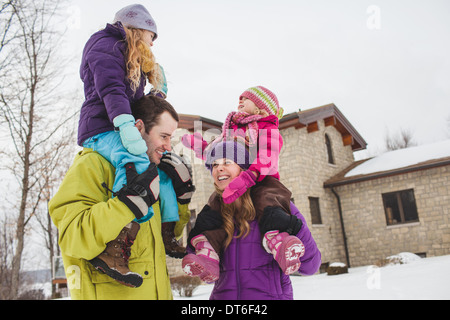 Mutter und Vater tragen Töchter im Schnee Stockfoto