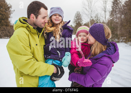 Mutter und Vater tragen Töchter im Schnee Stockfoto