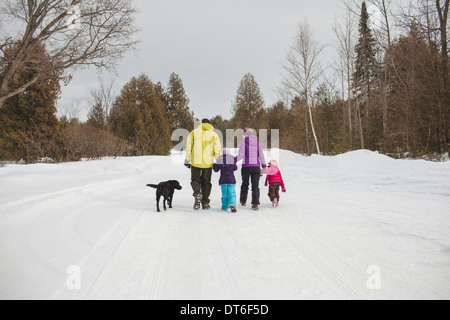 Mutter und Vater mit zwei Kindern und Hund, Wandern im Schnee, Rückansicht Stockfoto