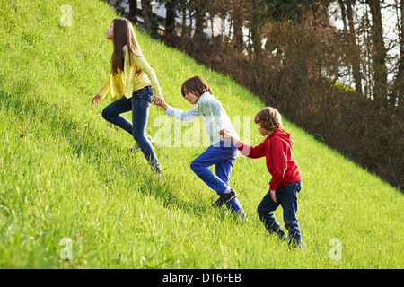 Schwester und jüngere Brüder Klettern auf Wiese Stockfoto