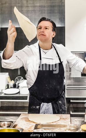 Chef wirft Pizzateig Mitte Luft in Großküchen Stockfoto