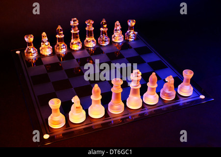 Glas-Schach auf einem Schachbrett von einem bunten blauen und orangefarbenen Licht beleuchtet und auf ein Glas Schachbrett Stockfoto