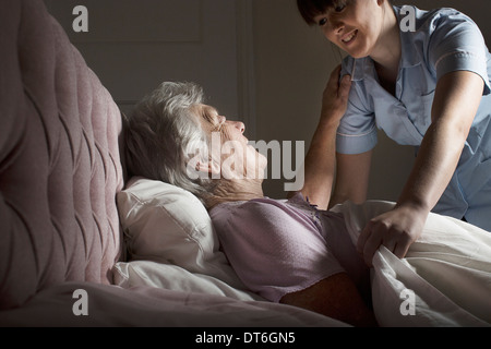 Körperpflege-Assistent im Gespräch mit älteren Frau im Bett Stockfoto