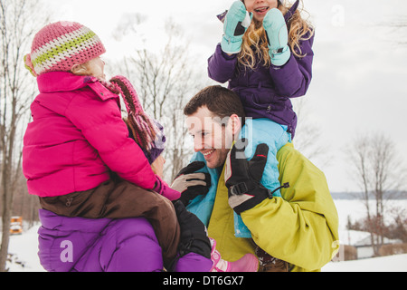 Mutter und Vater tragen Töchter im Schnee Stockfoto