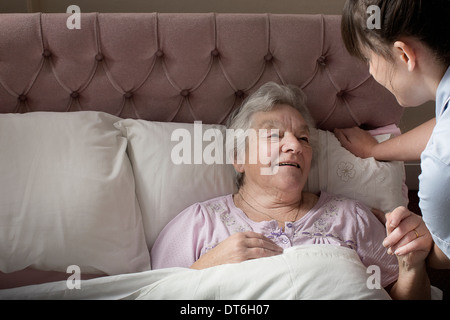 Körperpflege-Assistent im Gespräch mit älteren Frau im Bett Stockfoto