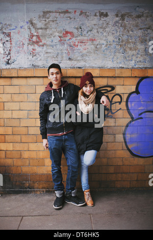 In voller Länge Portrait von gut aussehenden jungen Mann stehend mit seine schöne Freundin an eine Wand gelehnt. Stockfoto
