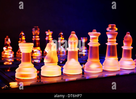 Glas-Schach auf einem Schachbrett von einem bunten blauen und orangefarbenen Licht beleuchtet und auf ein Glas Schachbrett Stockfoto