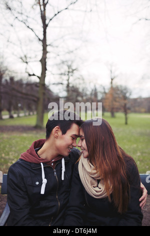 Teenager-Paar auf einer Bank sitzen und genießen einen Tag im Park. Schöne junge Paar im Park. Gemischte Rassen, männlich und weiblich. Stockfoto