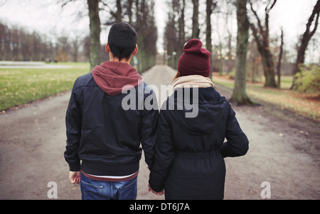 Rückansicht des Teenager-Paar im Park, die Hand in Hand gehen. Junger Mann und Frau in warme Kleidung im Freien. Stockfoto