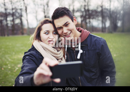 Lustige Teenager-paar fotografieren sich mit Ihrem Smartphone im Park.  Süße junge Mädchen mit ihrem Freund fotografieren. Stockfoto