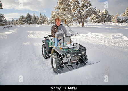 Eine Seniorin Pflüge Schnee mit einem ATV, all-Terrain-Fahrzeug, nach einem großen Schneesturm in Zentral-Oregon. Stockfoto