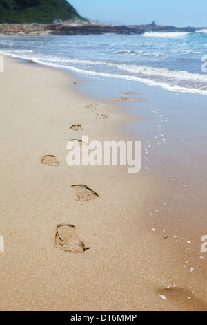 Menschliche Fußabdrücke am Strand Sand mit Meer im Hintergrund führt in Richtung des Betrachters Stockfoto