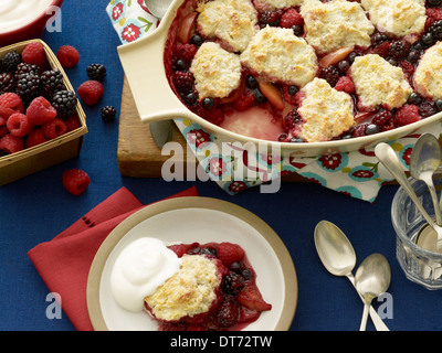 Gemischte Beeren Schuster mit Erdbeeren, Brombeeren und Himbeeren serviert mit einem Klecks Creme auf einem blauen Hintergrund mit einem re Stockfoto